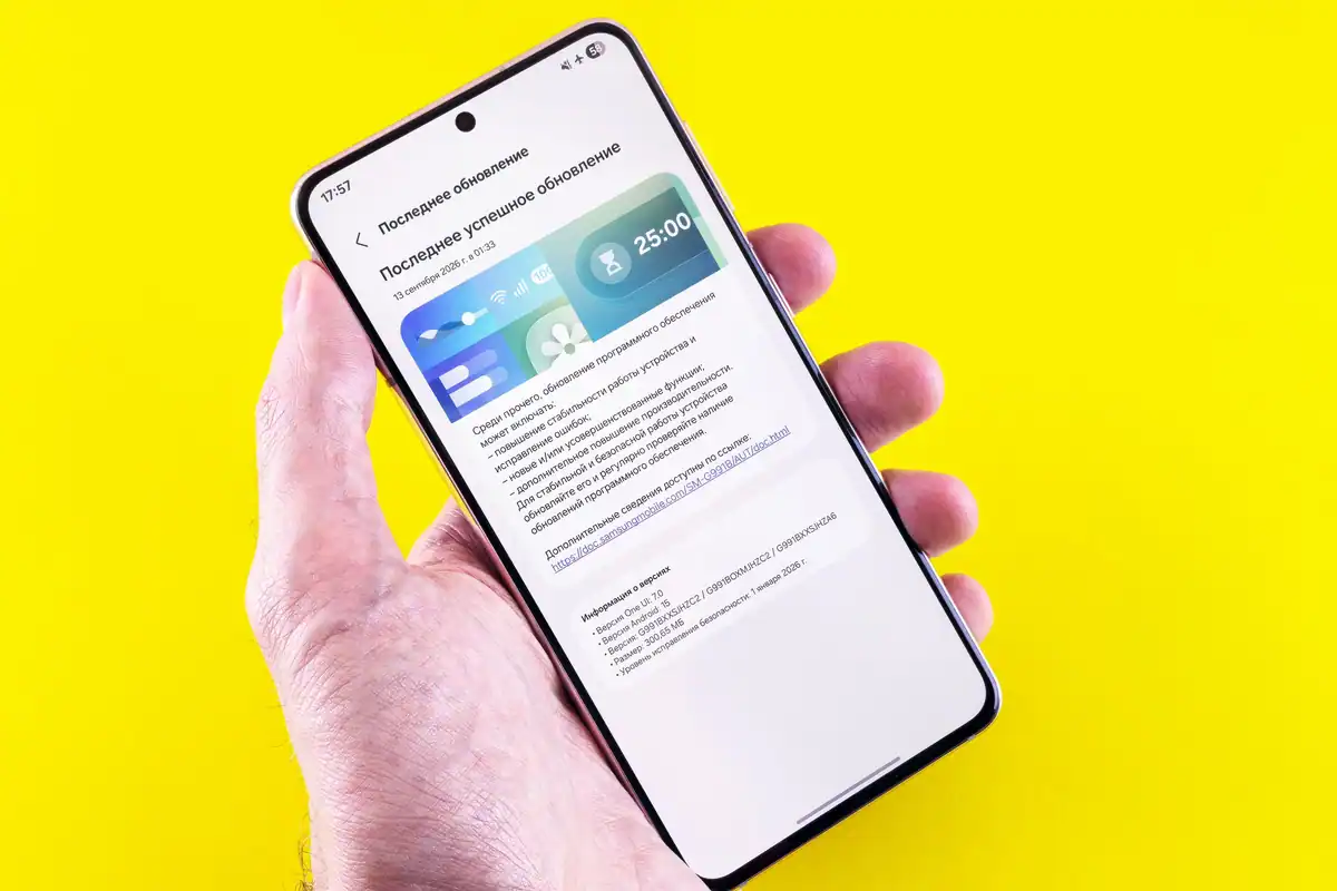 Mână care ține un telefon pe al cărui ecran apare o notificare de actualizare, pe fundal galben