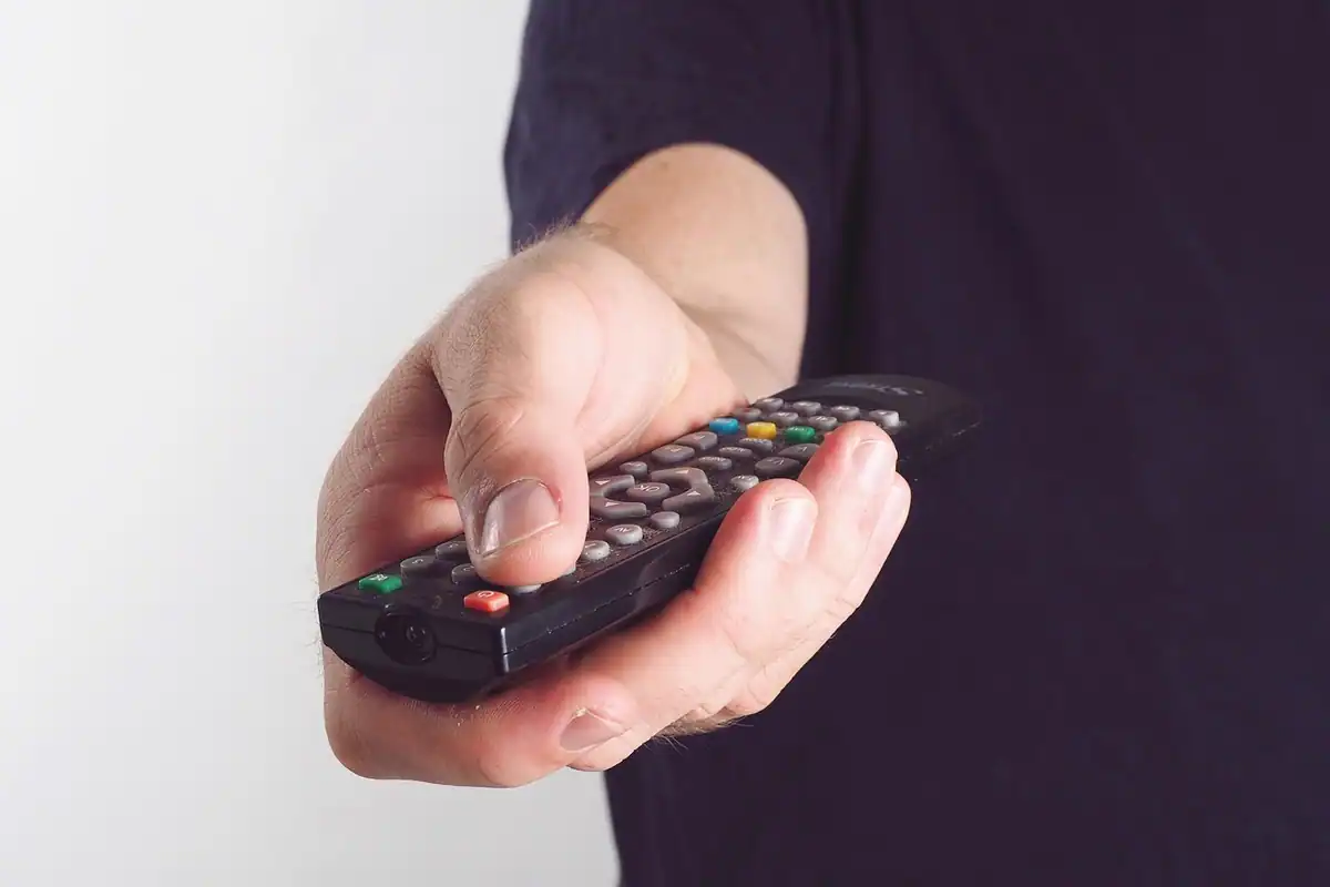 Mână care ține o telecomandă și alege următorul program de la televizor