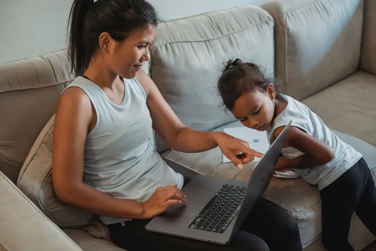 Mamă și fiică care navighează pe internet cu un netbook, pe canapea, în sufragerie, ziua