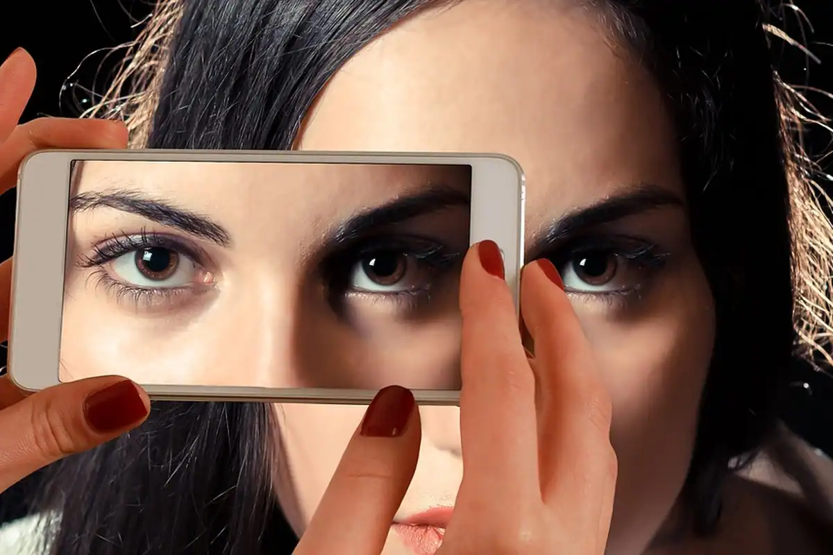 Smartphone ținut în mână, cu camera frontală îndreptată spre fața unei femei pentru deblocare