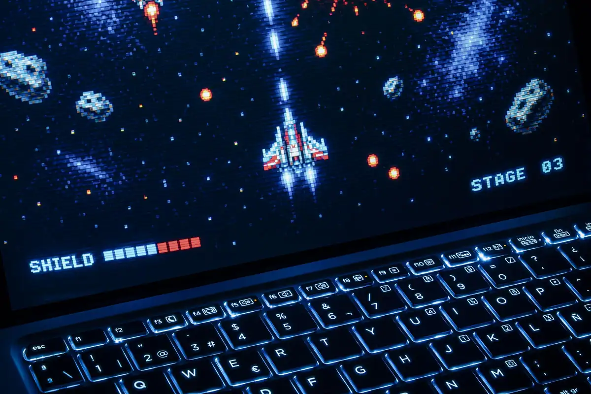 Laptop cu tastatură iluminată, având pe ecran un joc arcade retro cu grafică pixelată