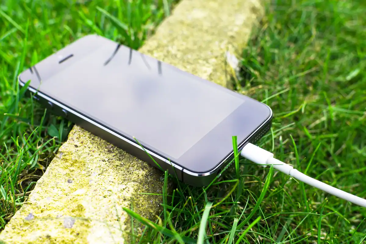 Telefon conectat la un cablu de încărcare, așezat pe iarbă, în aer liber