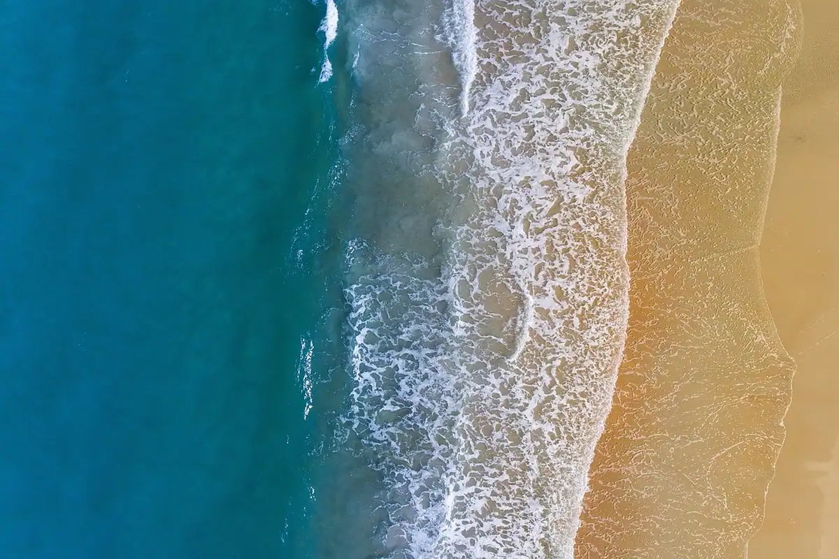 Valuri înspumate pe o plajă văzută din dronă, la granița dintre uscat și ocean