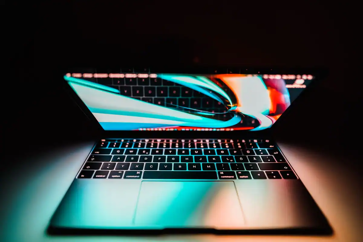 Laptop deschis cu ecranul colorat reflectat pe tastatură, pe un fundal întunecat
