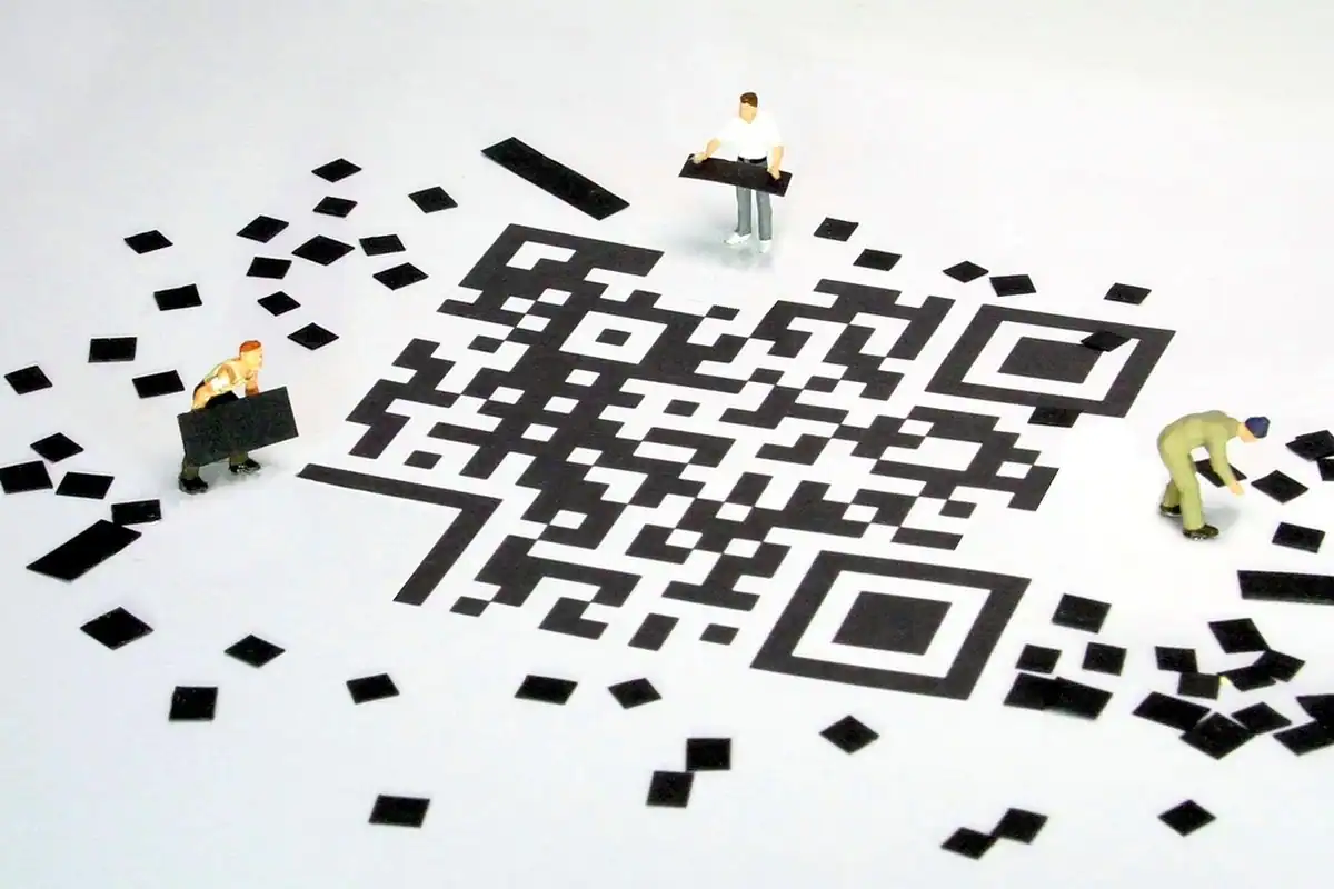 Cod QR mare din pătrățele negre, așezat de figurine miniaturale de muncitori
