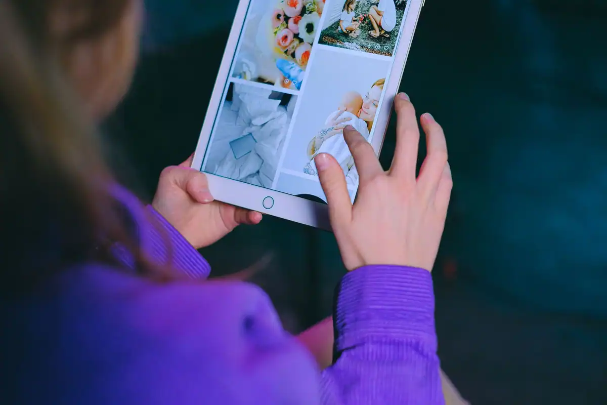 Femeie care privește fotografiile de pe ecranul unei tablete, așezată într-o cameră