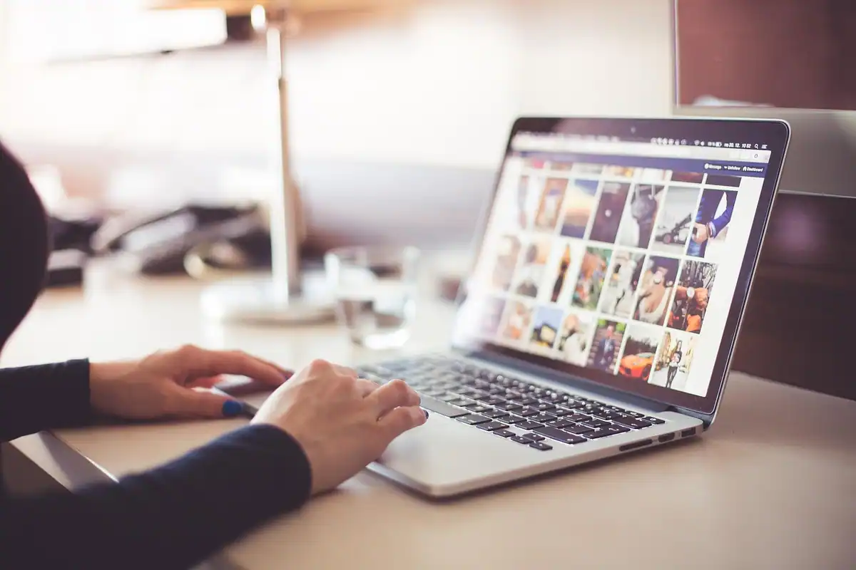 Mâini care tastează pe un laptop deschis la o pagină plină de imagini