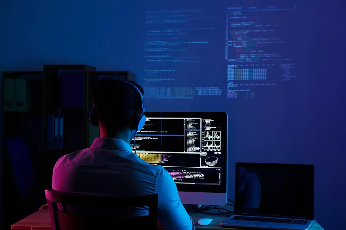 Programator care lucrează noaptea la mai multe monitoare cu linii de cod