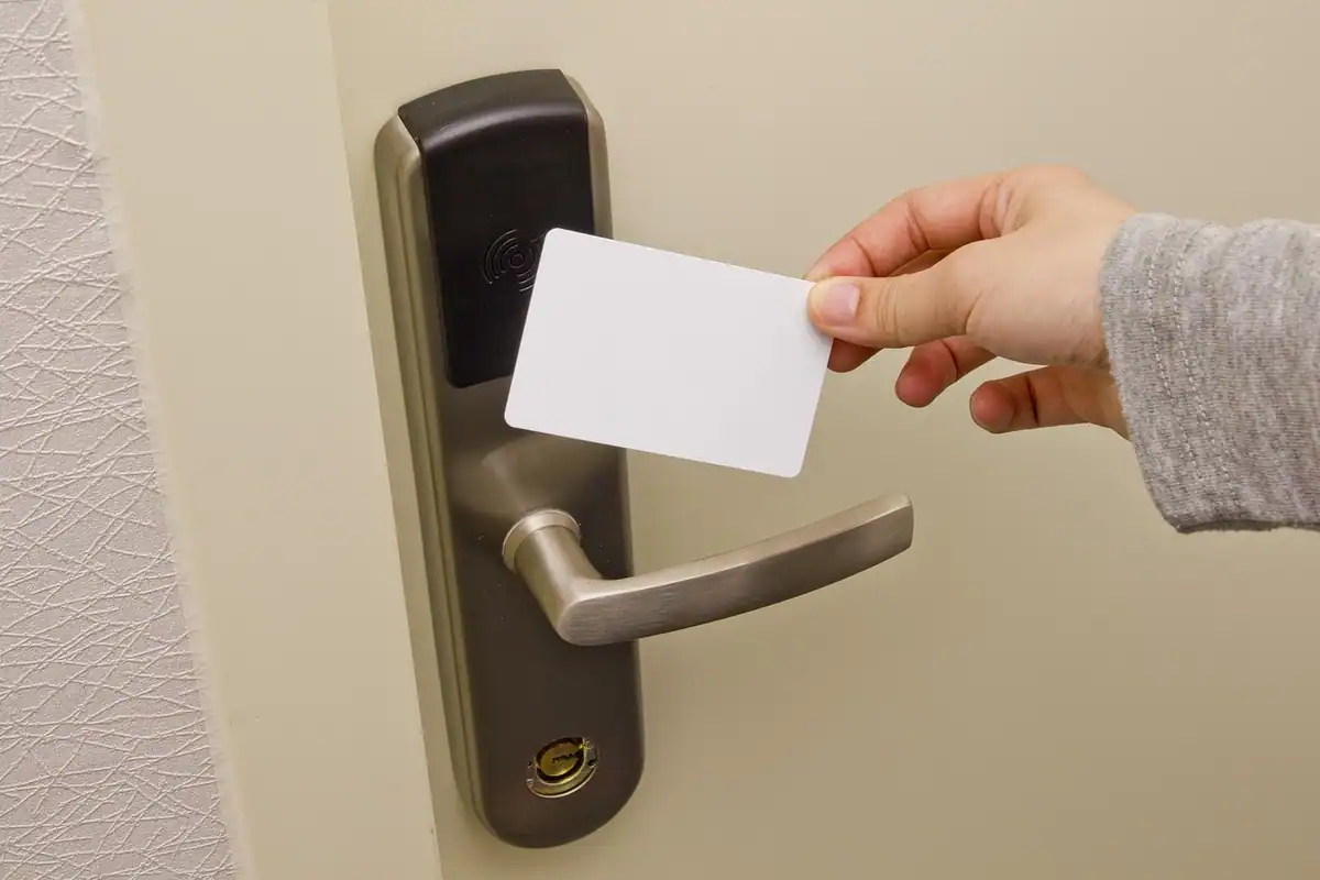 Mână care apropie un card de acces de încuietoarea electronică a unei uși