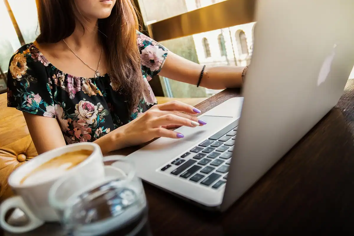 Tânără care lucrează pe laptop într-o cafenea, lângă o ceașcă de cafea