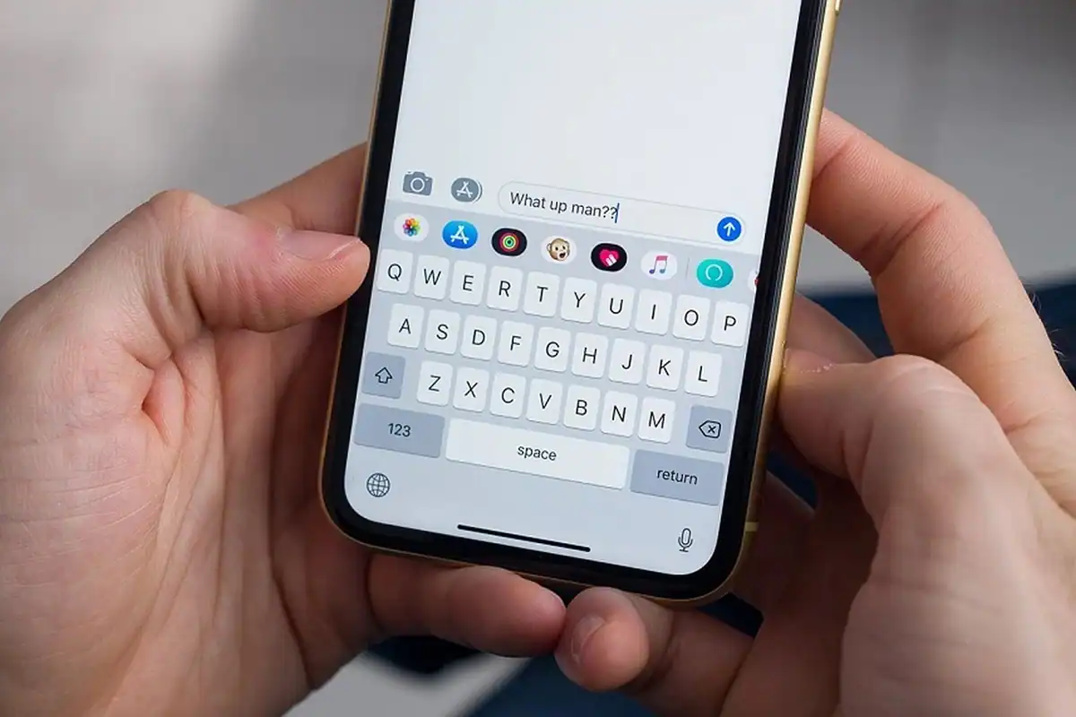 Mâini care scriu un mesaj pe tastatura de pe ecranul unui telefon