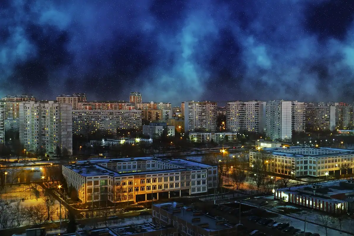 Clădiri de apartamente cu ferestre luminate noaptea într-un oraș, cu nori deasupra acoperișurilor