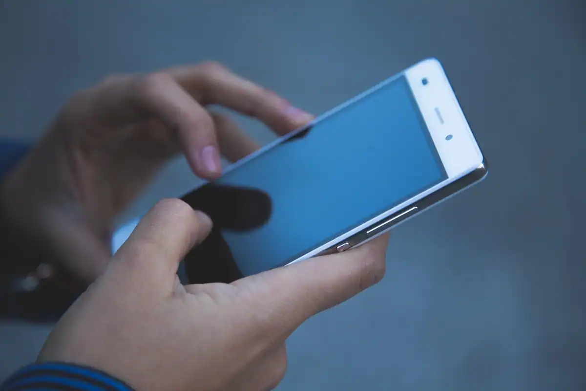 Mâini care țin un smartphone cu ecranul albastru aprins