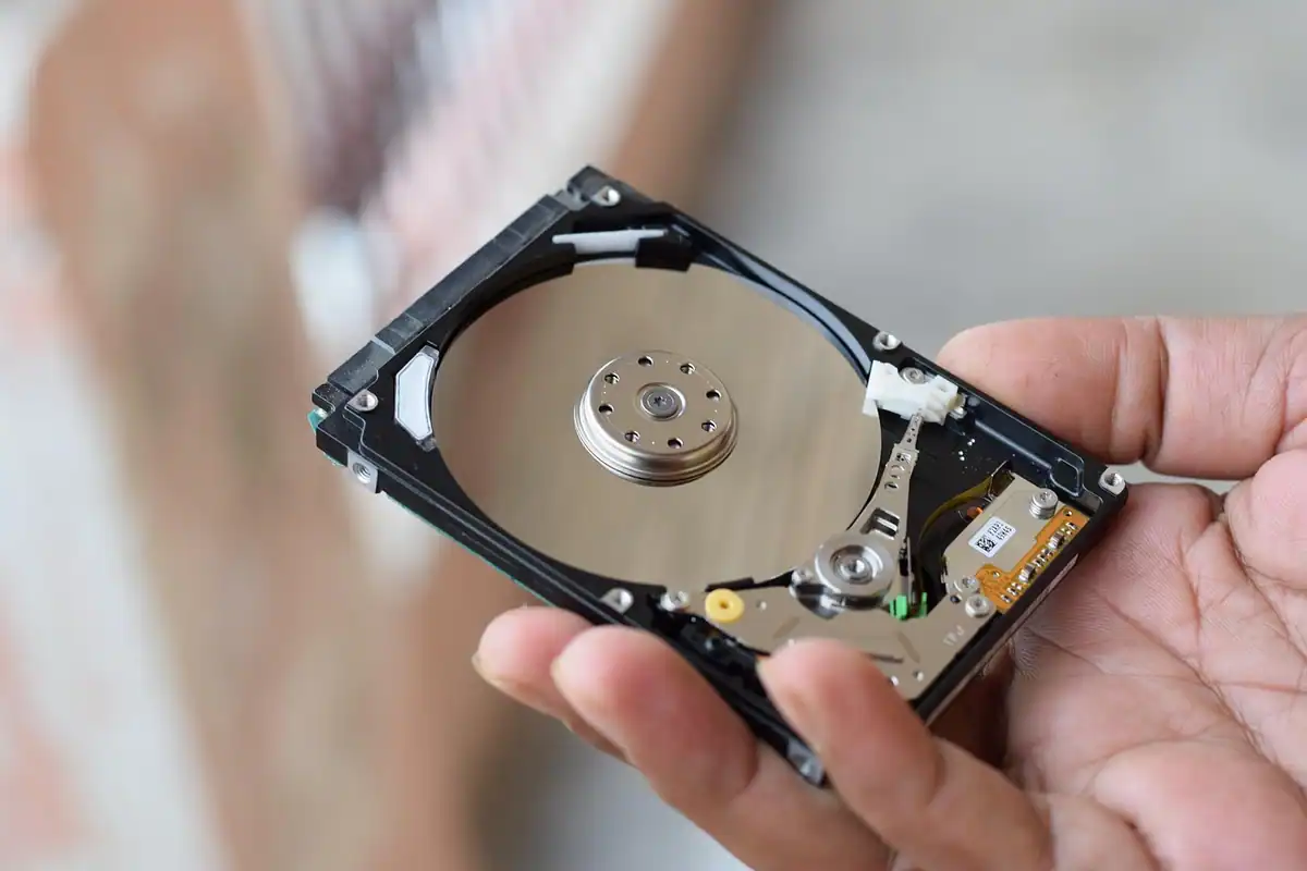Hard disk deschis ținut în mână, cu platanul și capul de citire vizibile
