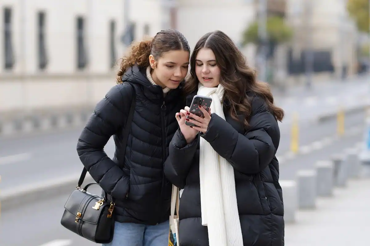 Două tinere care se uită împreună la un telefon pe stradă