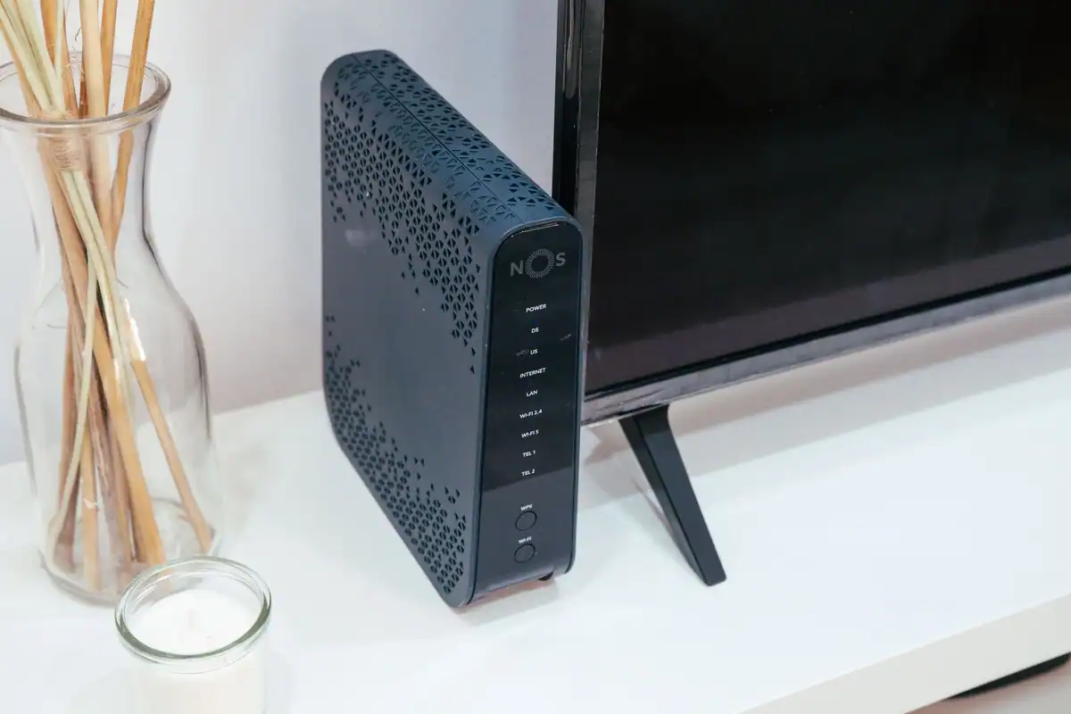 Router Wi-Fi într-un living modern, lângă un televizor și un obiect decorativ din sticlă