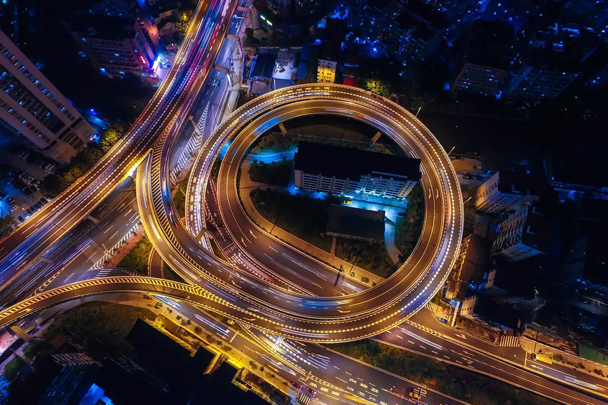 Nod rutier circular văzut de sus noaptea, cu drumuri luminate și trafic între cartiere