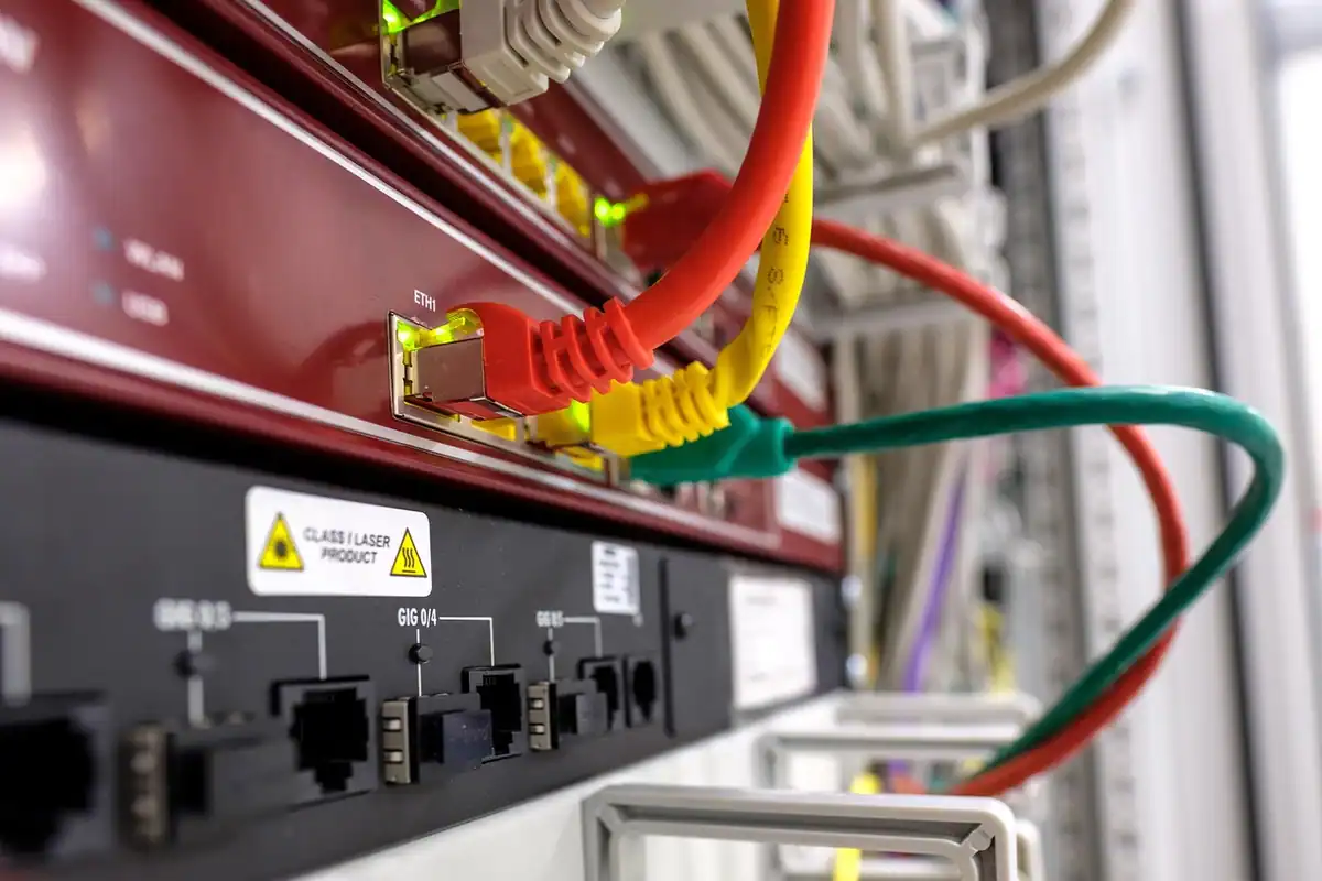 Router Wi-Fi cu cabluri de rețea conectate, așezat pe un raft, lângă alte echipamente