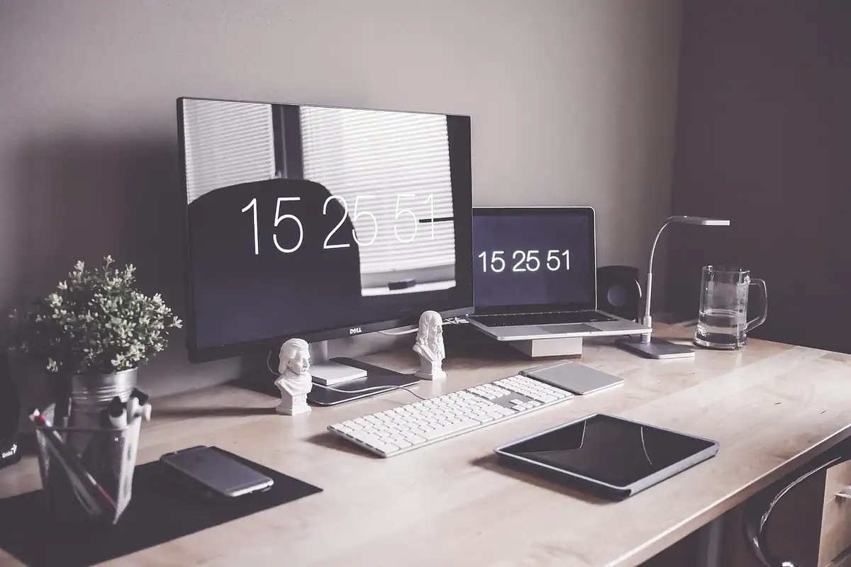 Birou cu monitor, laptop, tabletă și telefon care afișează aceeași oră