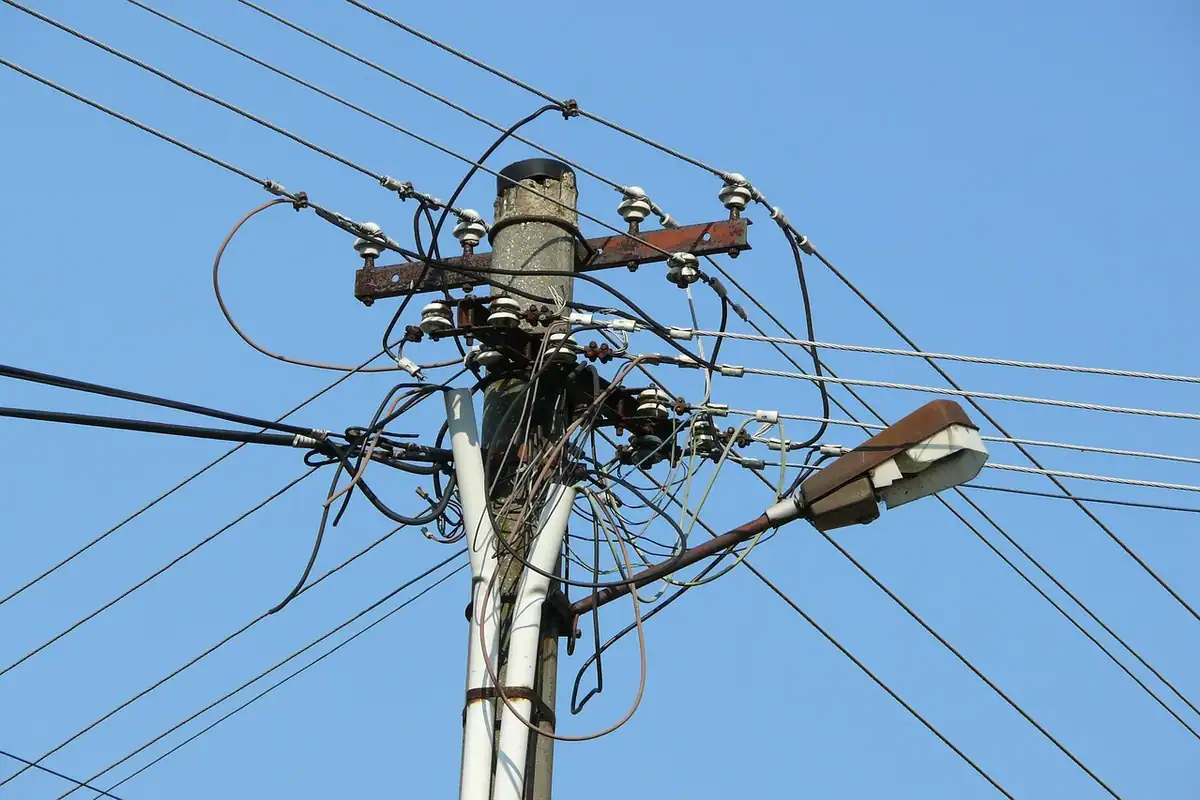 Stâlpi de electricitate cu cabluri întinse pe cer, la marginea unui sat