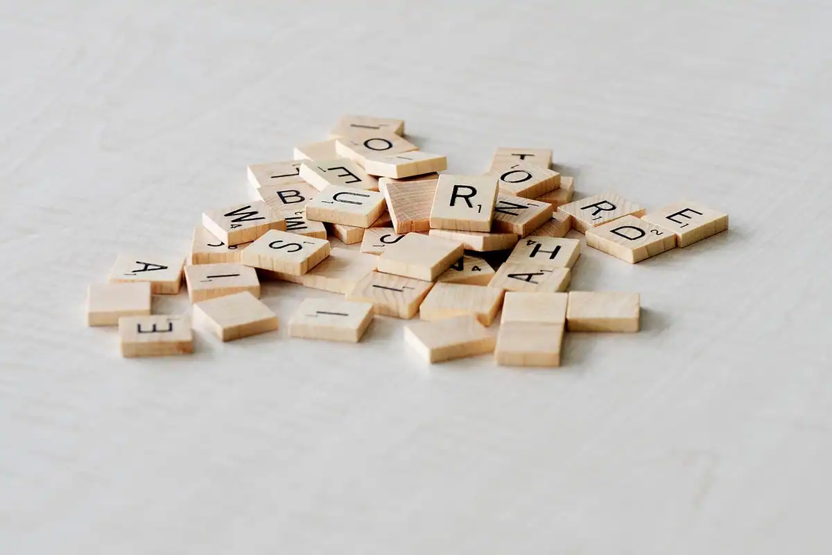 Litere de Scrabble împrăștiate pe o masă, din care se pot forma cuvinte